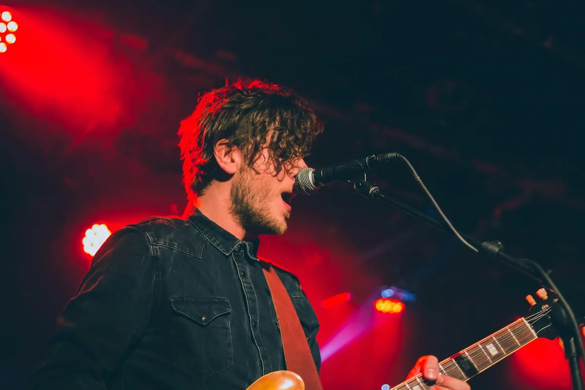 Independent artist singing into a microphone on stage under red lights